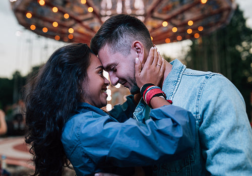 Smiling couple embracing at night against carousel in an amusement park