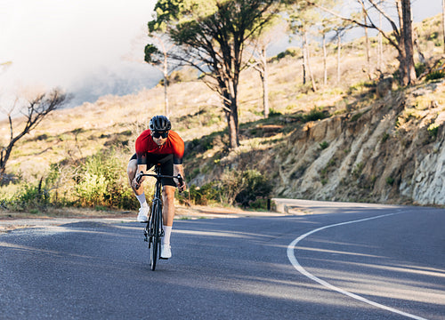 Professional triathlon athlete riding a road bike. Male cyclist riding down his bicycle on an empty road.