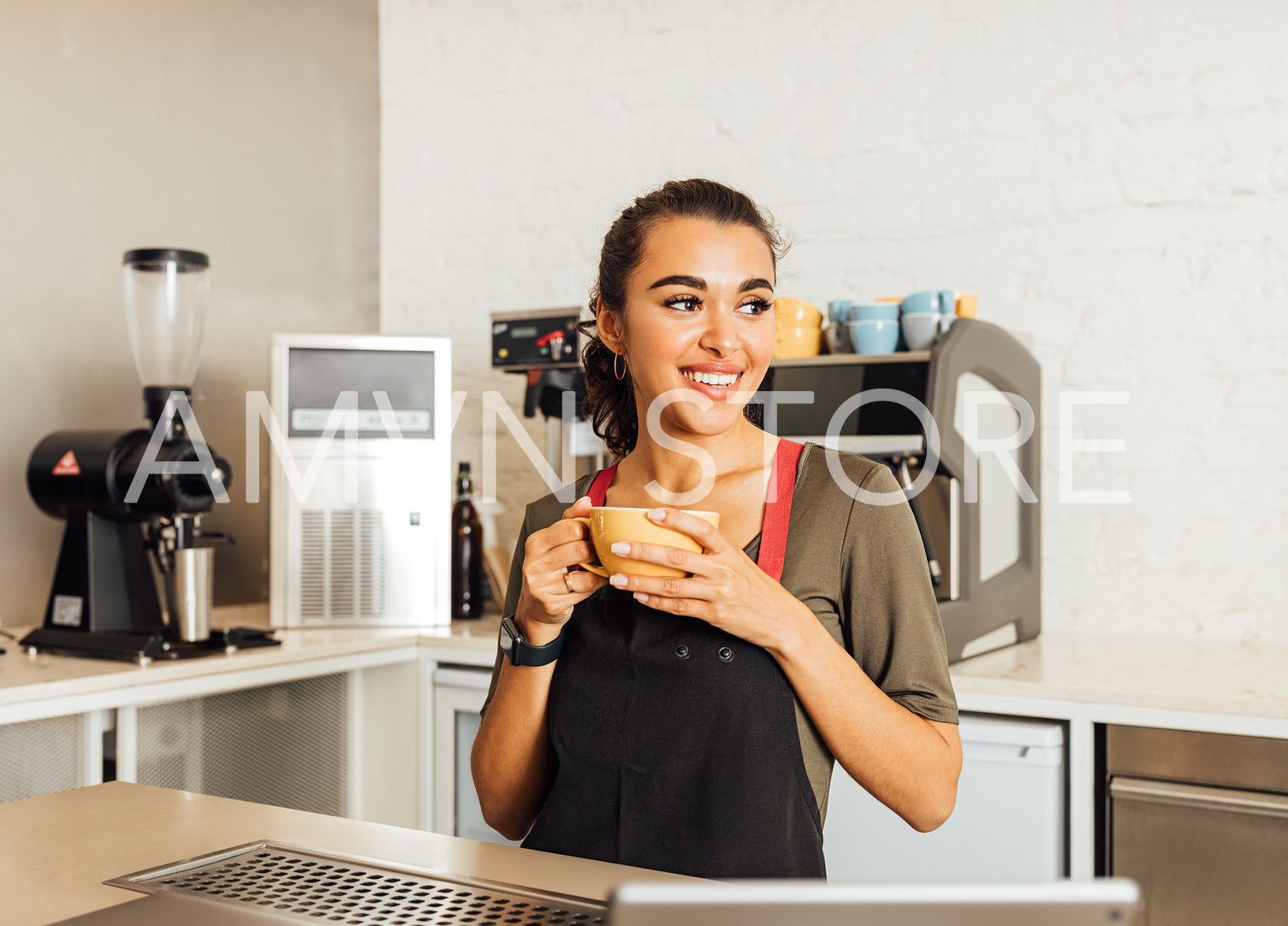 Smiling female barista looking away, holding a coffee mug in cafe	