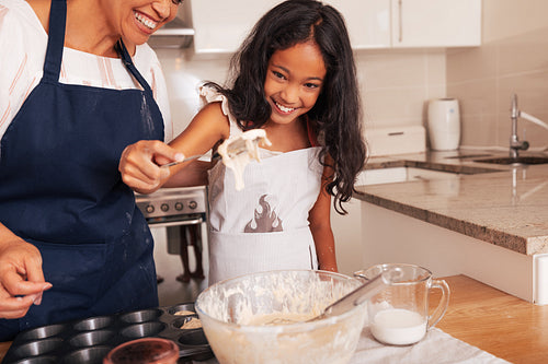 Granny and granddaughter cook together. Happy girl holding a spoon with dough on it.