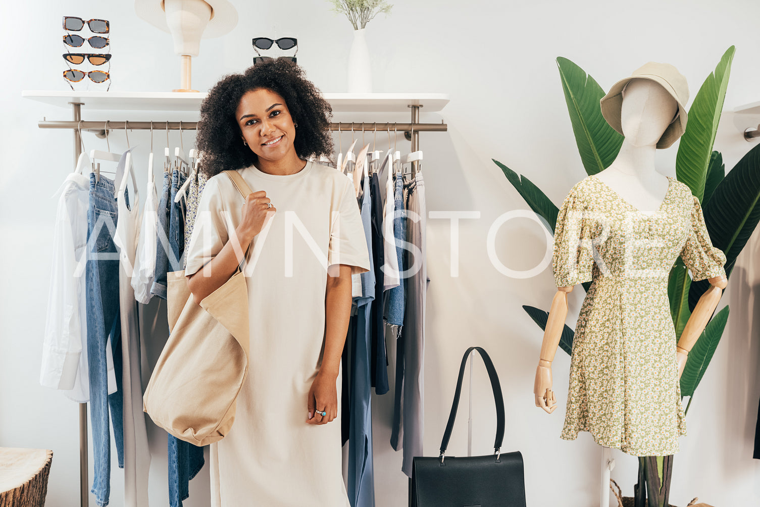 Portrait of a stylish woman with shopping bag standing at rack in boutique looking at camera