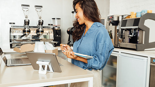 Side view of businesswoman in casuals standing in her coffee shop and making an accounting of goods.