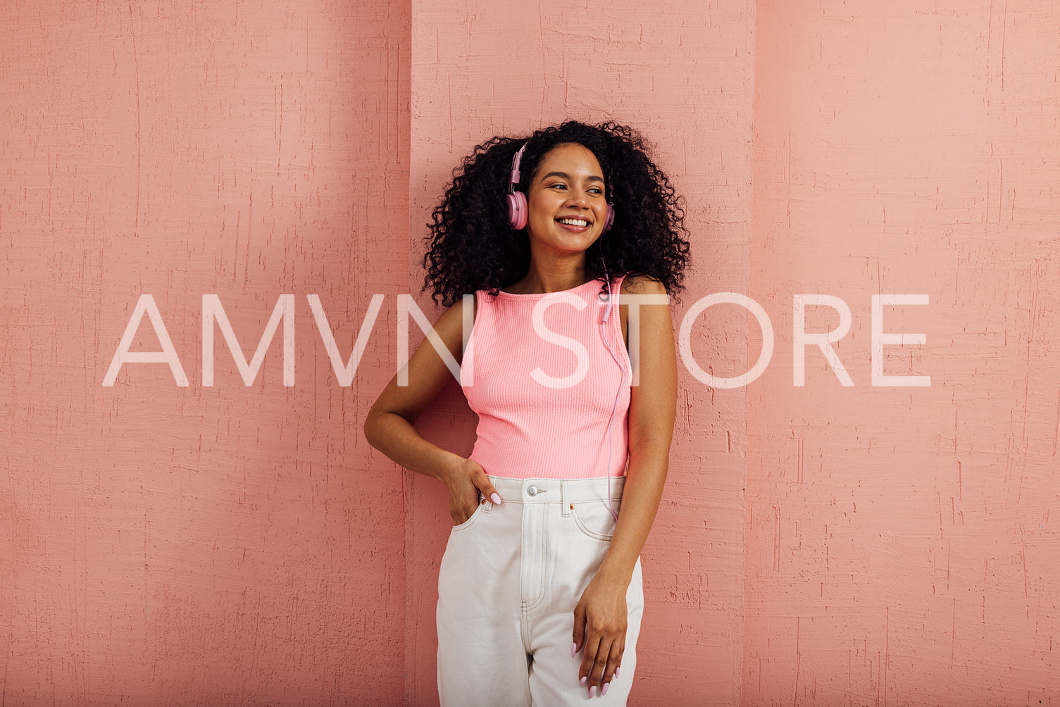 Smiling woman wearing pink headphones looking away leaning on wa