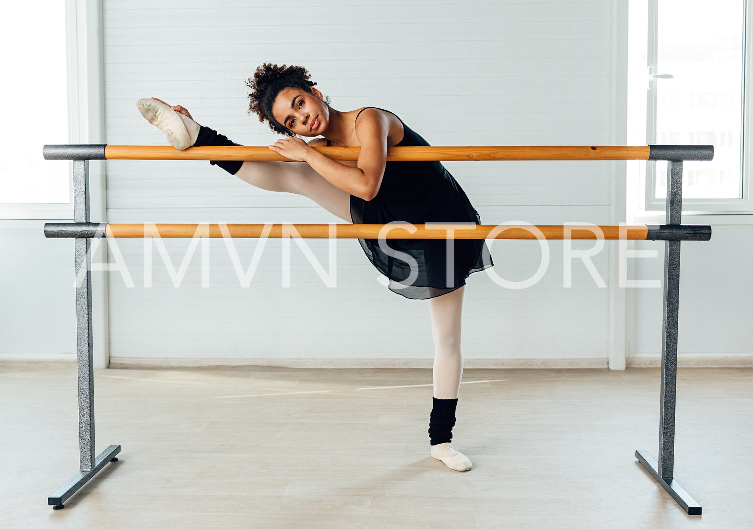 Young ballerina stretching her leg in dance studio. Woman doing exercise on ballet barre.	