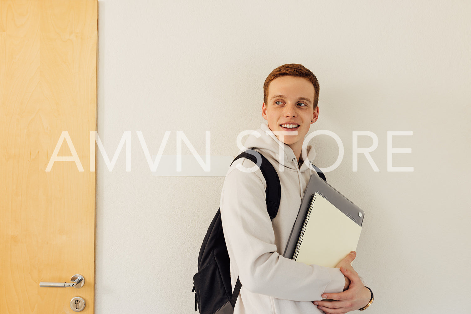 Smiling university student with backpack and textbooks leaning wall