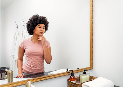 Beautiful young woman inspecting her skin in the bathroom mirror at home