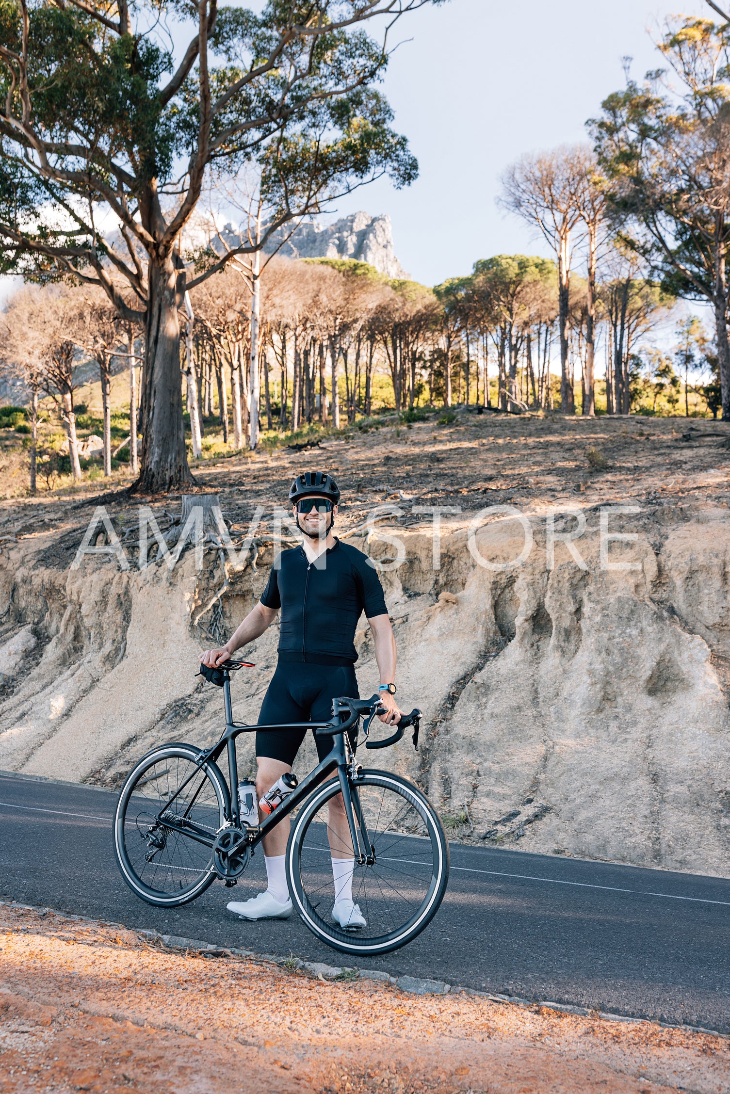 Full length of a smiling triathlete with bicycle standing on an empty road and looking at camera