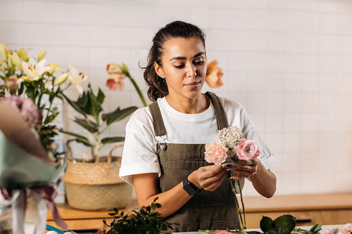 Woman standing at table making a bouquet of fresh flowers. Female florist working in flower shop.