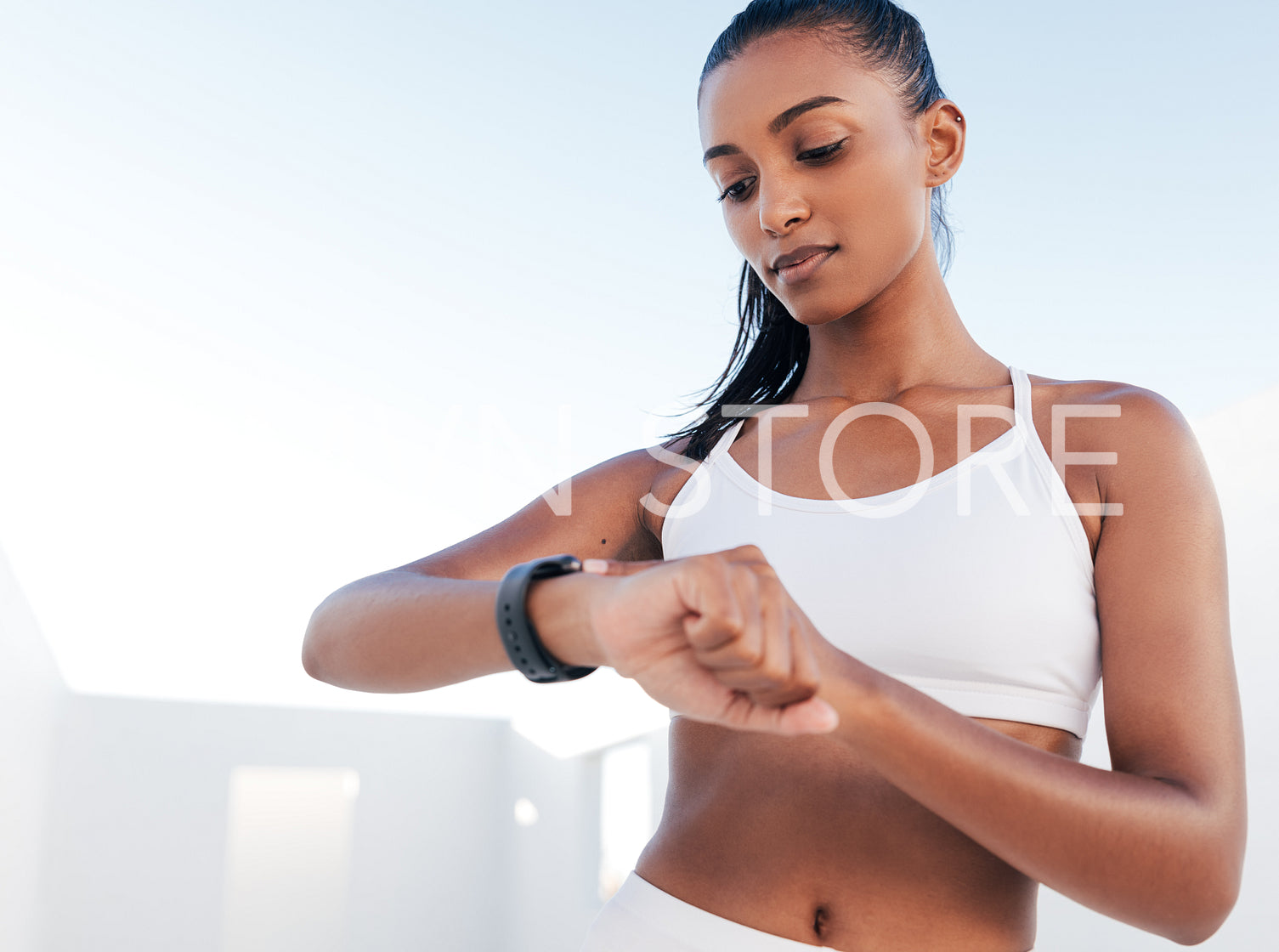 Slim female athlete looking at smartwatch. Woman in white fitness clothes standing outdoors checking her heart rate.