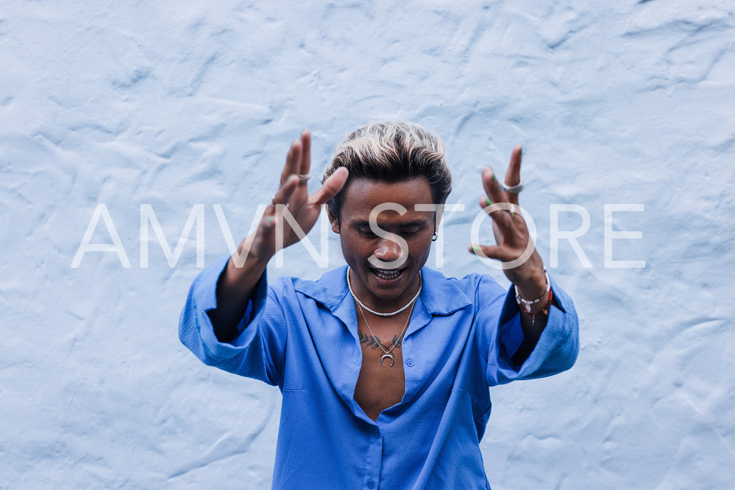 Young guy in blue shirt posing against a wall oudoors