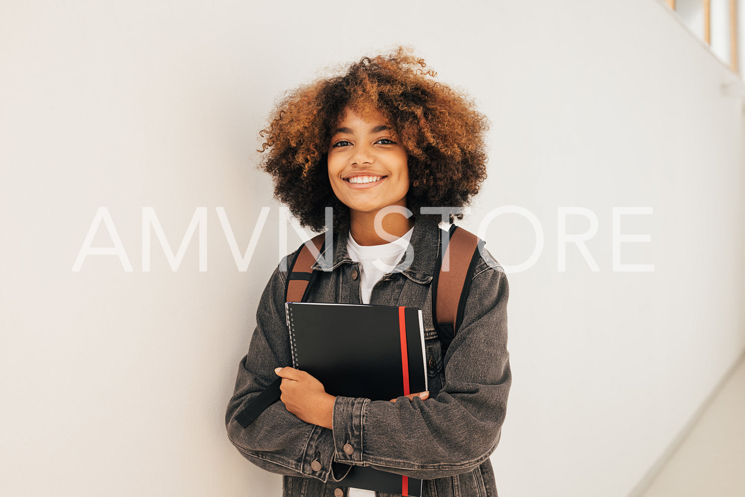 Happy girl with textbook standing at wall in school looking at camera