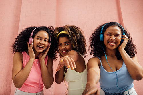 Three laughing women with curly hair dancing together and looking at camera, wearing headphones