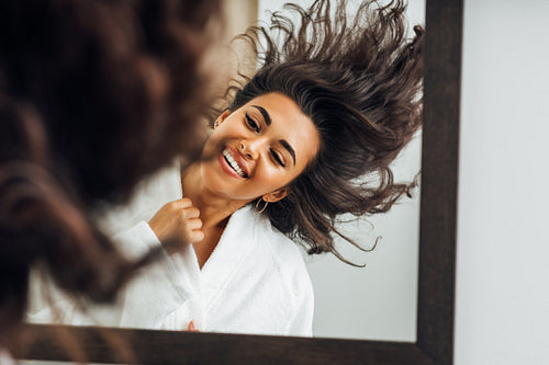 Portrait of a young happy woman playing with her hair in front of a bathroom mirror