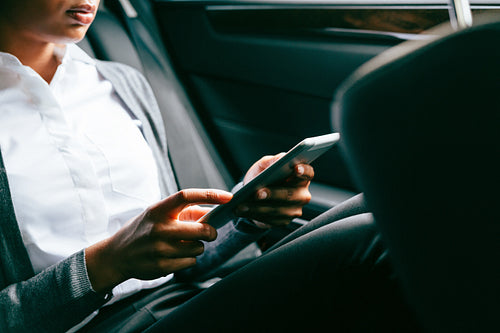 Unrecognizable woman using digital tablet, sitting on back seat of a car