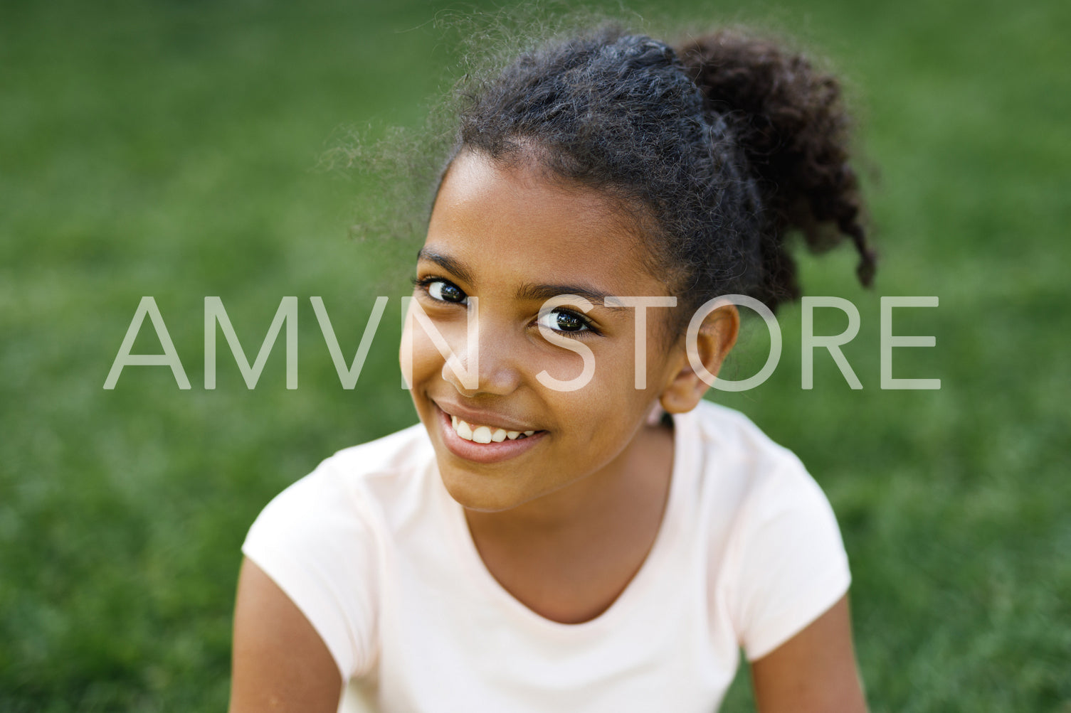 Smiling girl sitting on a grass in park, looking at camera