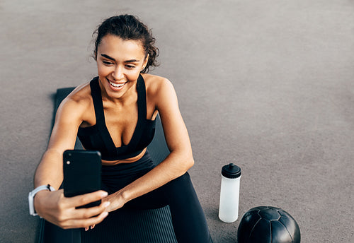 Smiling sportswoman live streaming from her cell phone while sitting on a mat outdoors