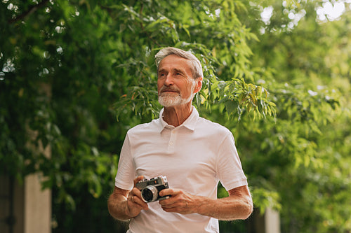 Mature photographer standing outdoors with a film camera and looking away