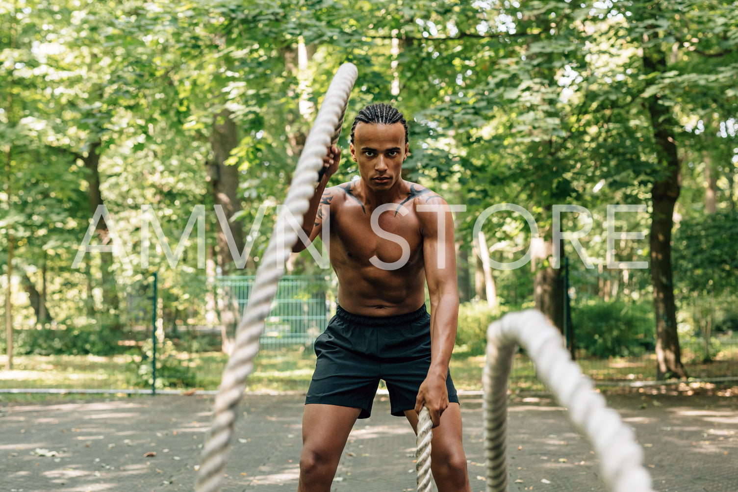 Bare chested man doing workout using battle ropes on the sports background outdoors	