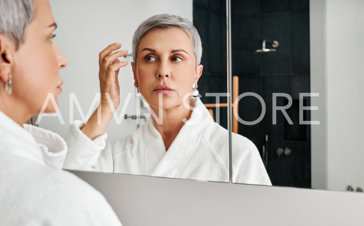 Mature woman adjusting her hairstyle in front of a mirror in bathroom