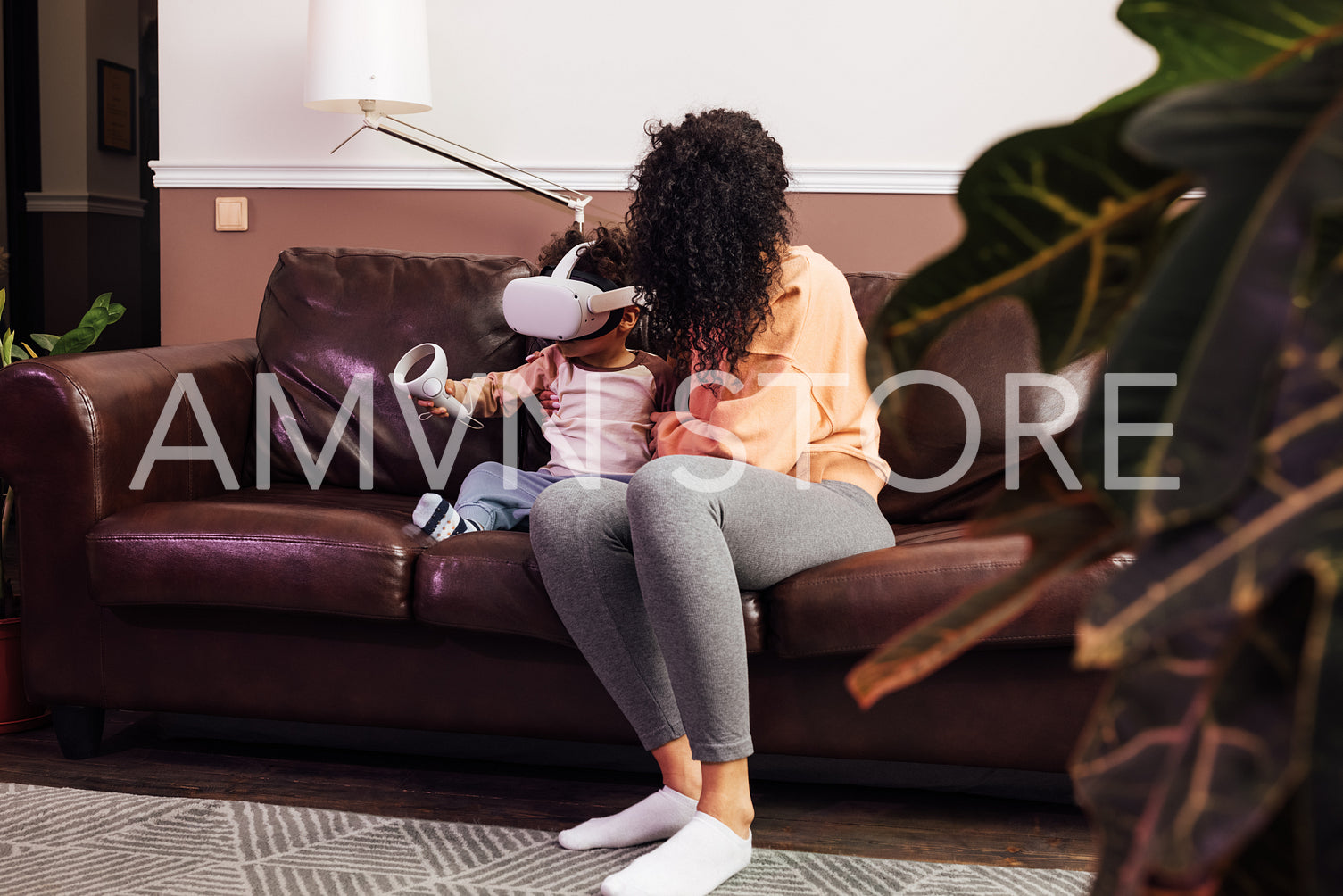 Young mother helping her son while he using VR set on sofa	