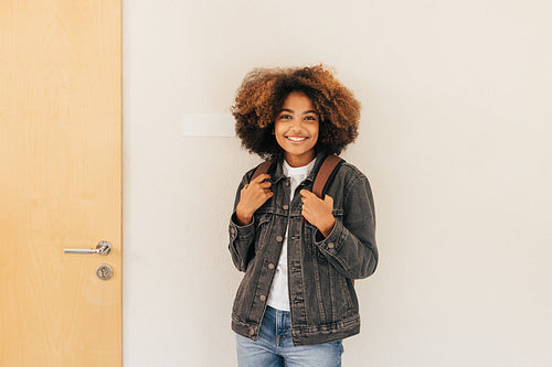 Portrait of a beautiful girl with curly hair. Student with backpack standing at wall.