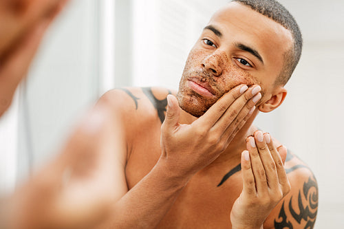 Handsome man applying natural scrub in front of a mirror