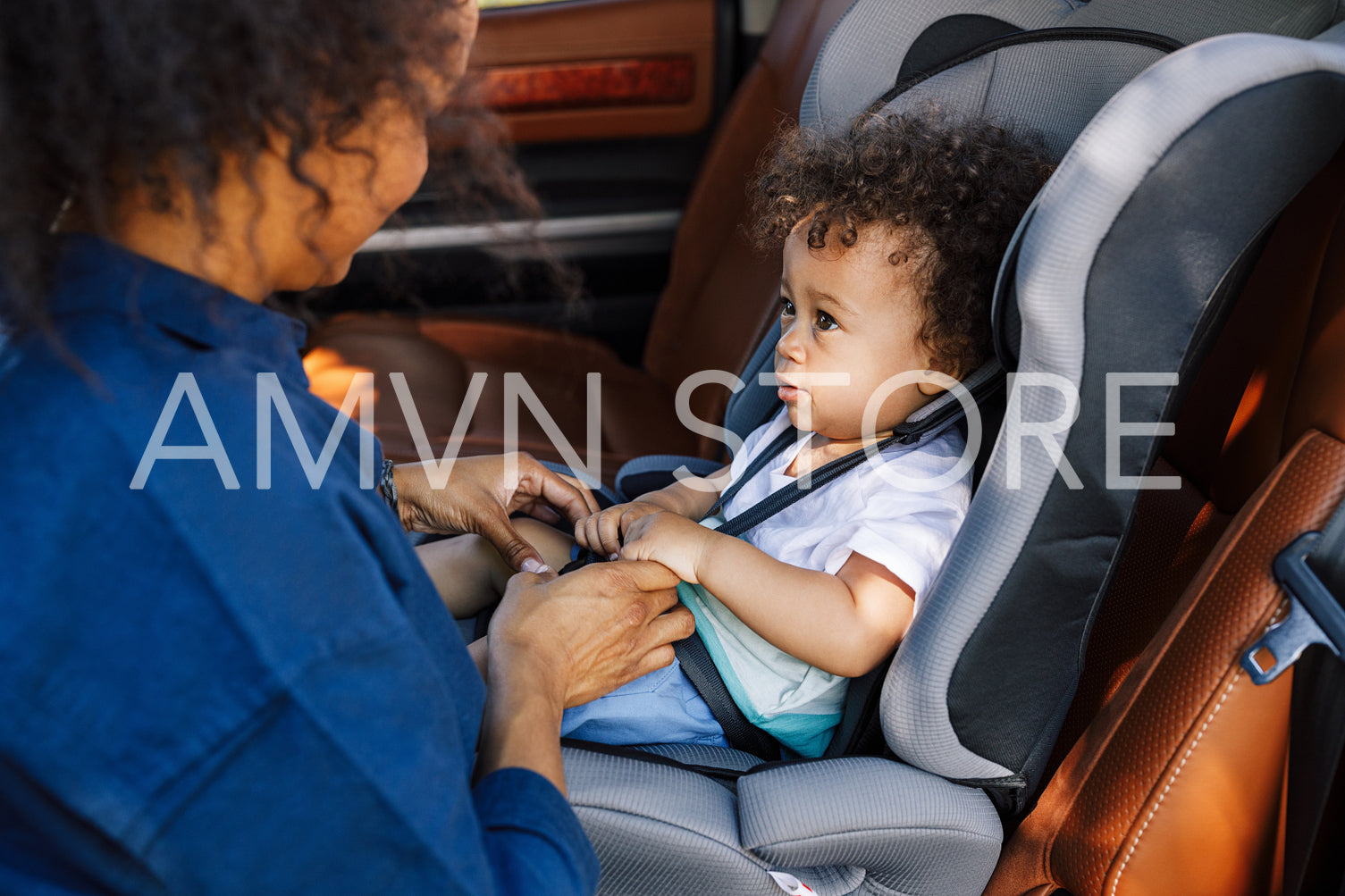 Young mother adjusting belts on a baby car seat. Toddler is looking at his mother while sitting in a car seat.