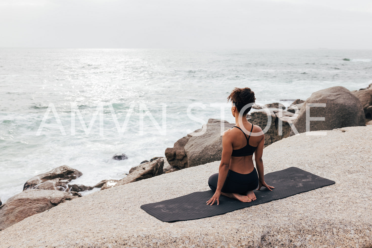 Back view of female in sportswear sitting in thunderbolt pose looking at ocean