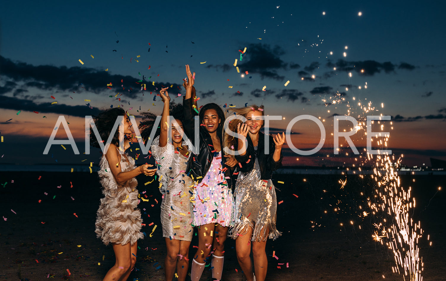 Happy friends celebrating outdoors at sunset. Four stylish women throwing confetti outdoors near fireworks.	