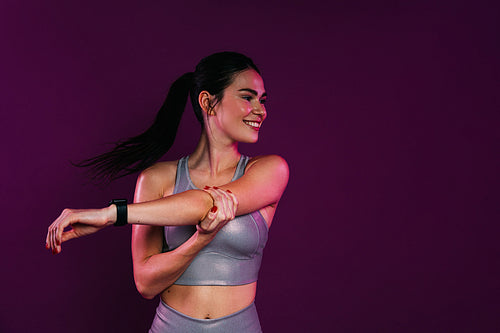 Young positive female flexing her hand while standing a magenta background