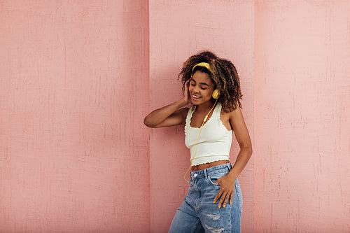 Young stylish woman wearing yellow headphones leaning a pink wal