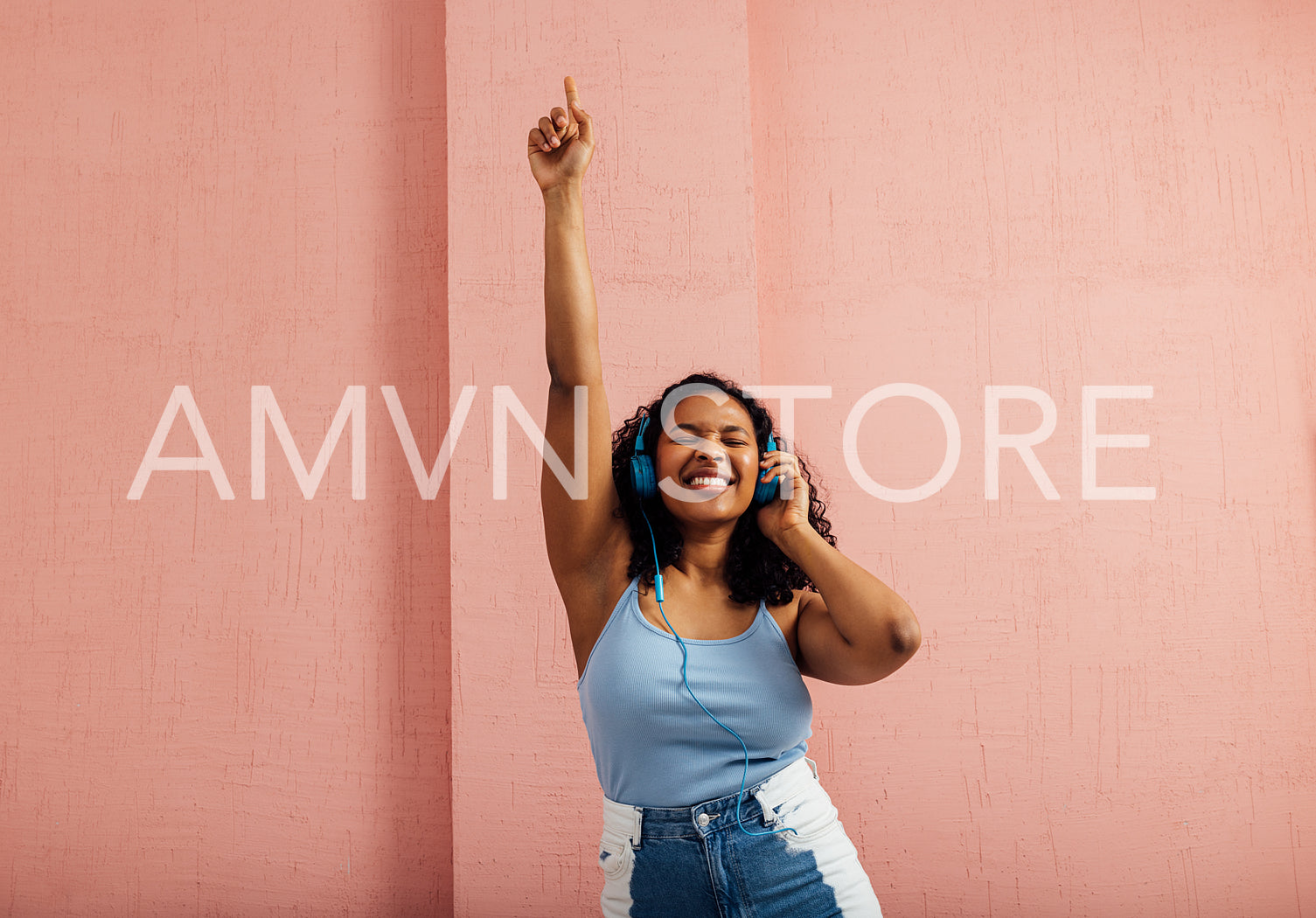 Plus size woman wearing blue headphones raise hand up and dancing against pink wall