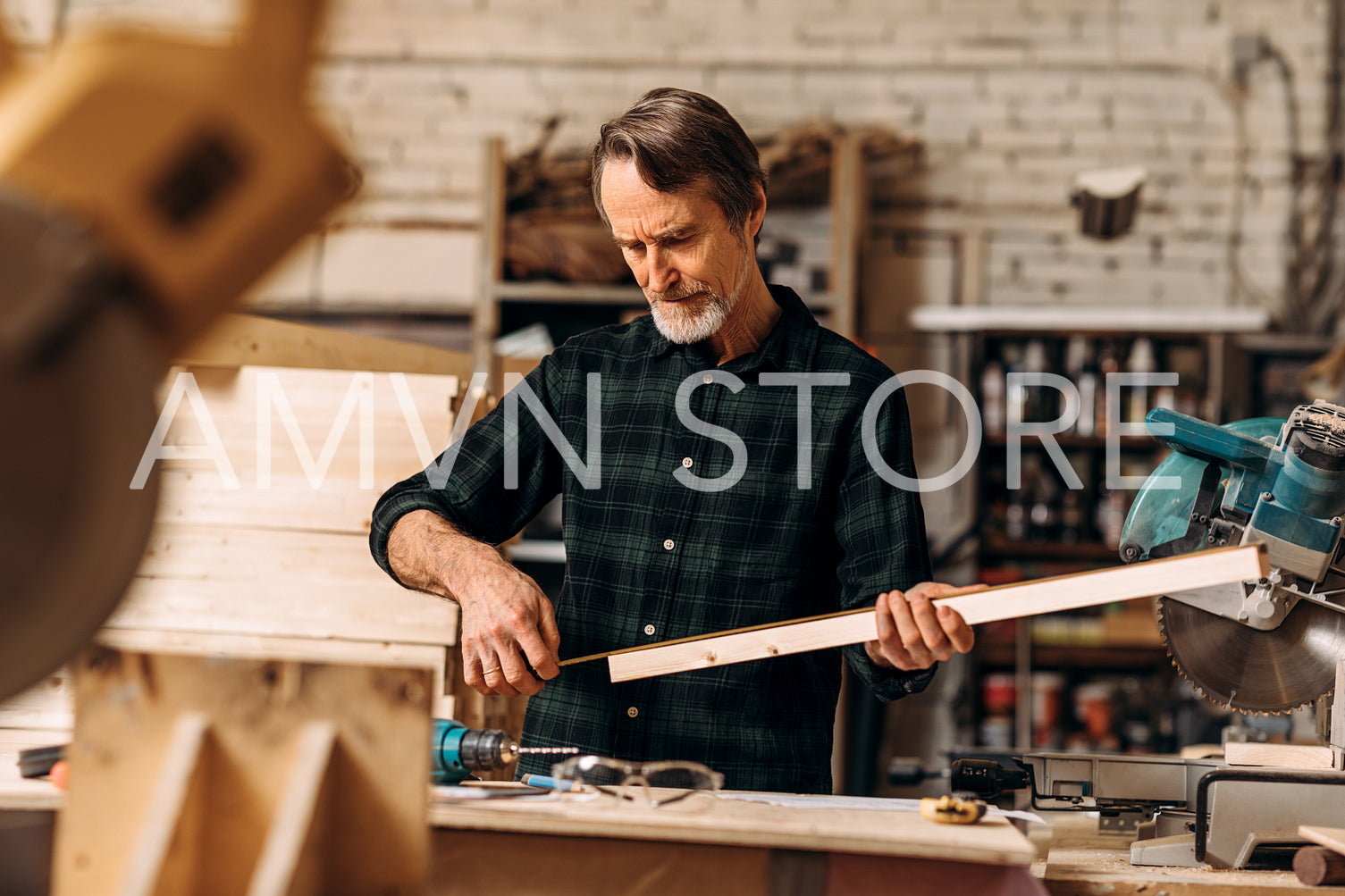 Male carpenter holding a wood plank and looking on measurement tape in a workshop	