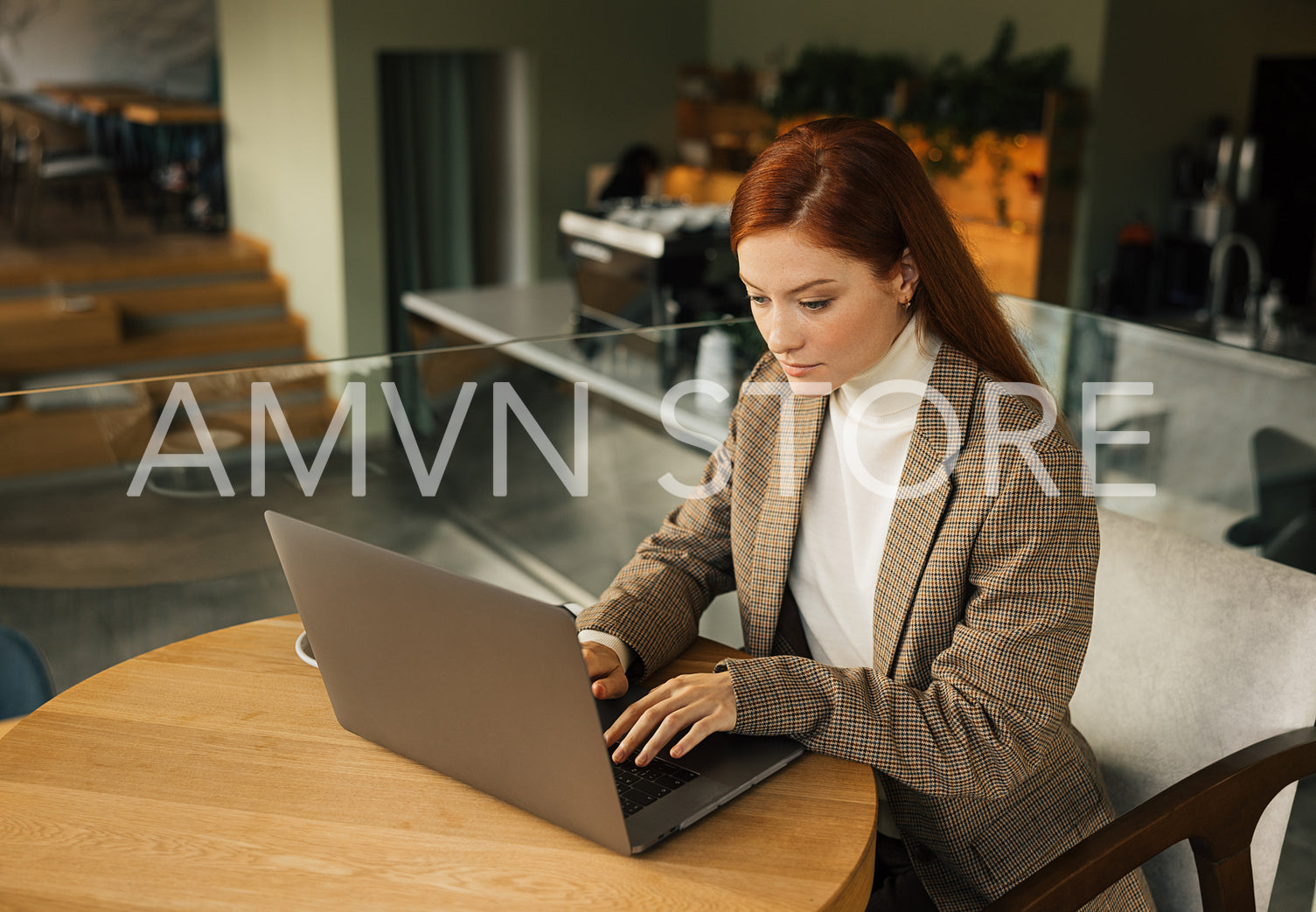 Businesswoman with ginger hair working in a cafe. Female typing on a laptop while sitting at a table in a cafe.