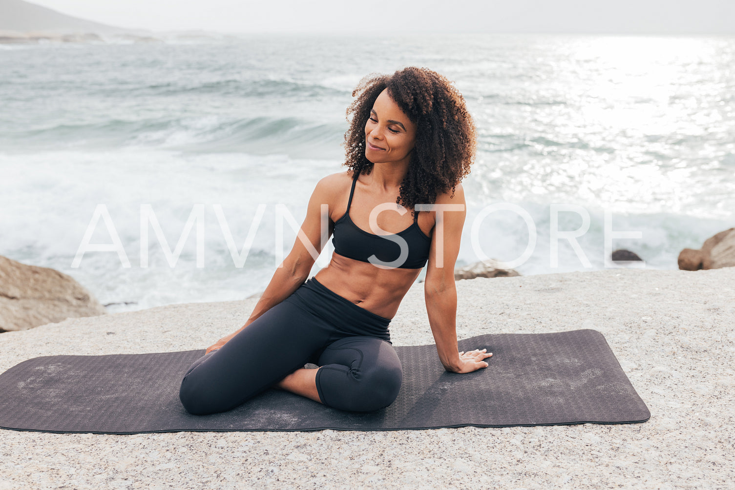 Smiling woman in fitness wear sitting on mat with closed eyes by bay