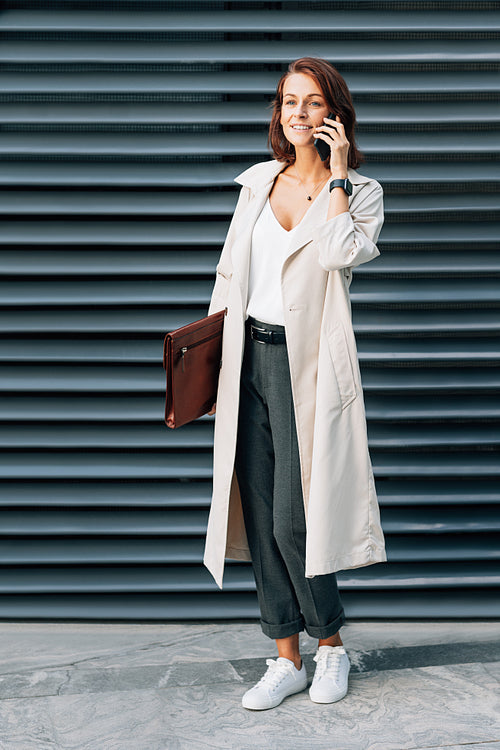 Full length of a stylish businesswoman with a folder talking on a mobile phone outdoors