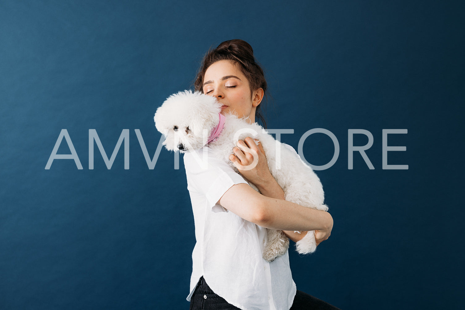 Young woman holding her little white dog in studio over blue bac