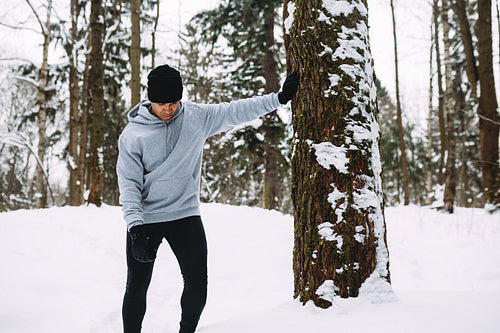 Tired athlete standing near a tree and resting after workout, looking down