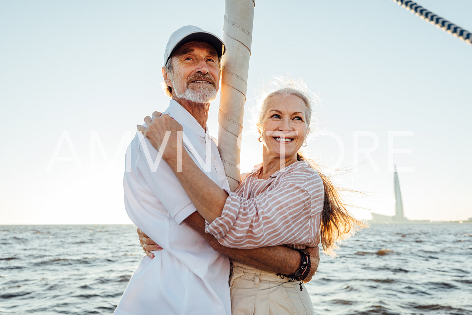 Two mature people standing at mast on sailboat and embracing each other	