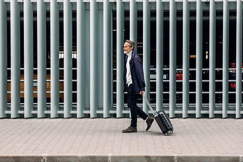 Side view of a man tourist walking with suitcase near a parking