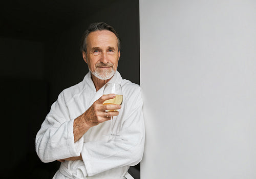 Portrait of a senior man leaning on a wall holding a glass of wine