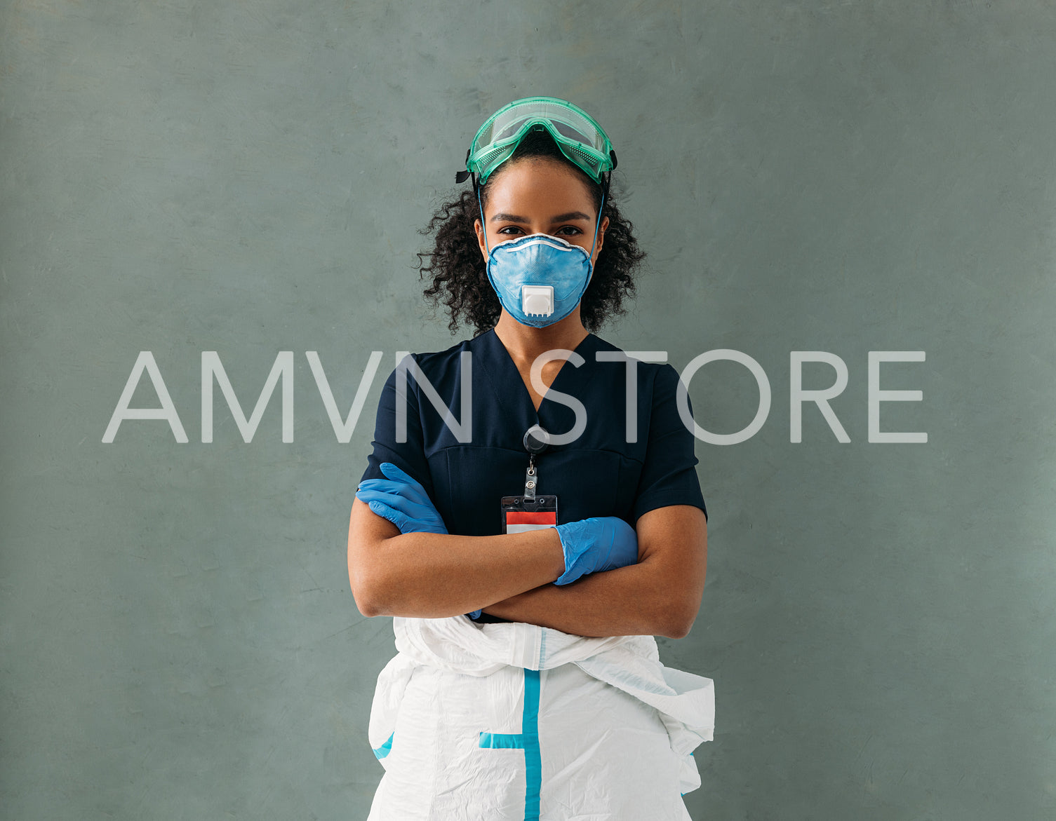 Young nurse wearing a protective glasses and respirator standing at wall with arms crossed	