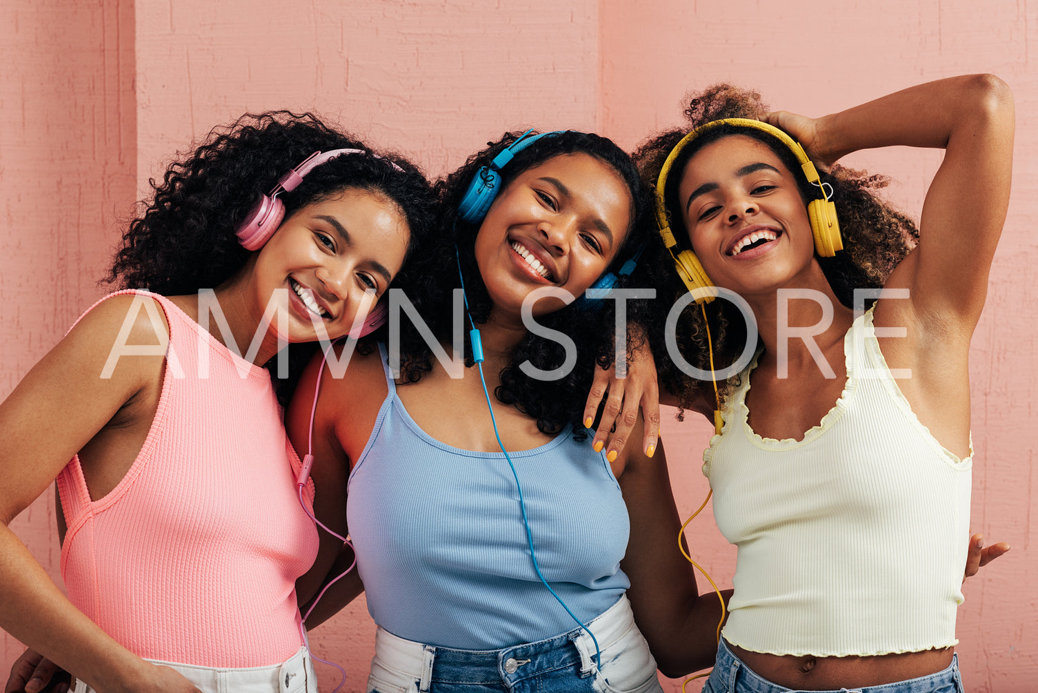 Portrait of three young women wearing headphones enjoying music against a pink wall