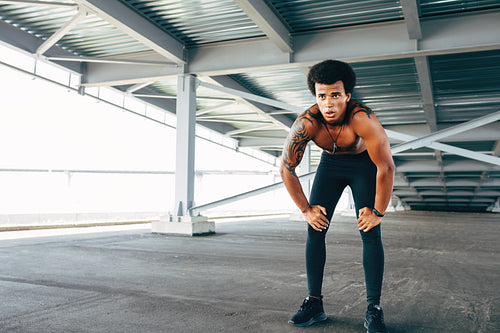 Muscular sportsman resting under a bridge with hands on his knees