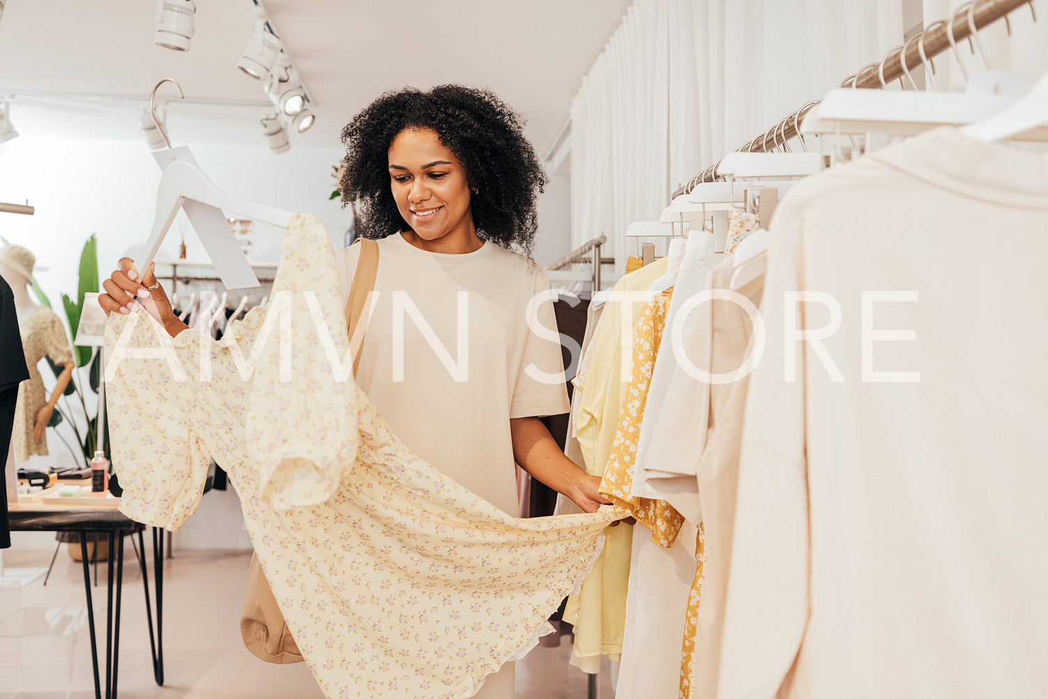 Young stylish woman standing in small boutique looking at dress she choose