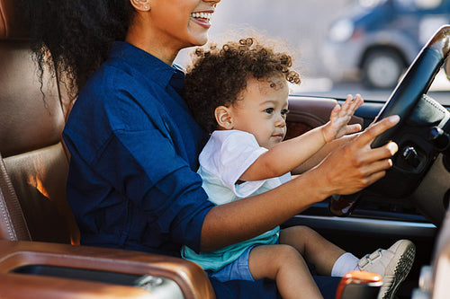 Smiling woman playing with son in a car holding the steering wheel