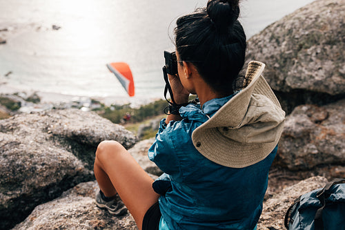 Woman sitting on the cliff making photographs on a film camera. Back view of female trekker resting on a mountain top with a camera.