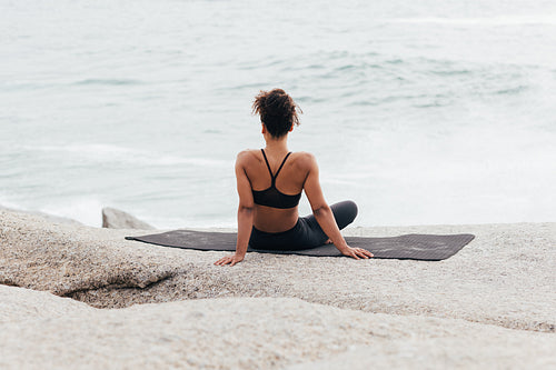 Woman looking at ocean while sitting on yoga mat