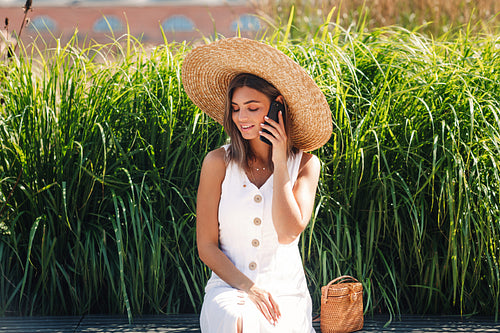 Young beautiful woman talking on a mobile phone while sitting in a park in front of a grass