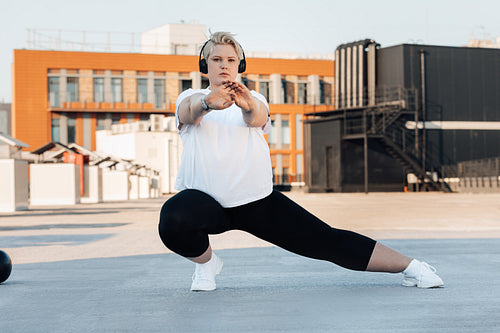 Plus size female in sportswear warming up body before training on the roof